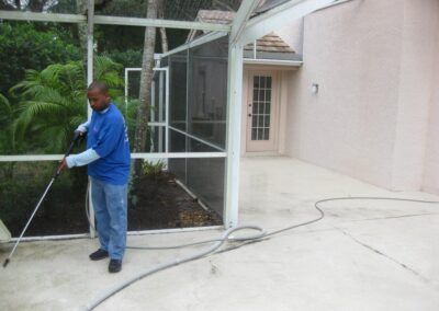 A man in blue shirt holding hose near tree.