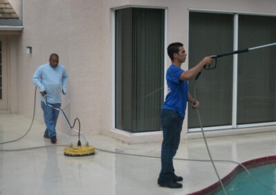 Two men are cleaning a pool with a power washer.
