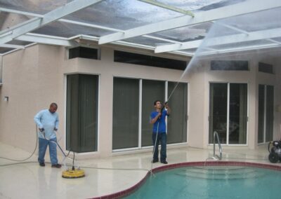 Two men cleaning a pool with a power washer.