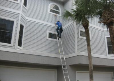 A man on a ladder painting the side of a house.